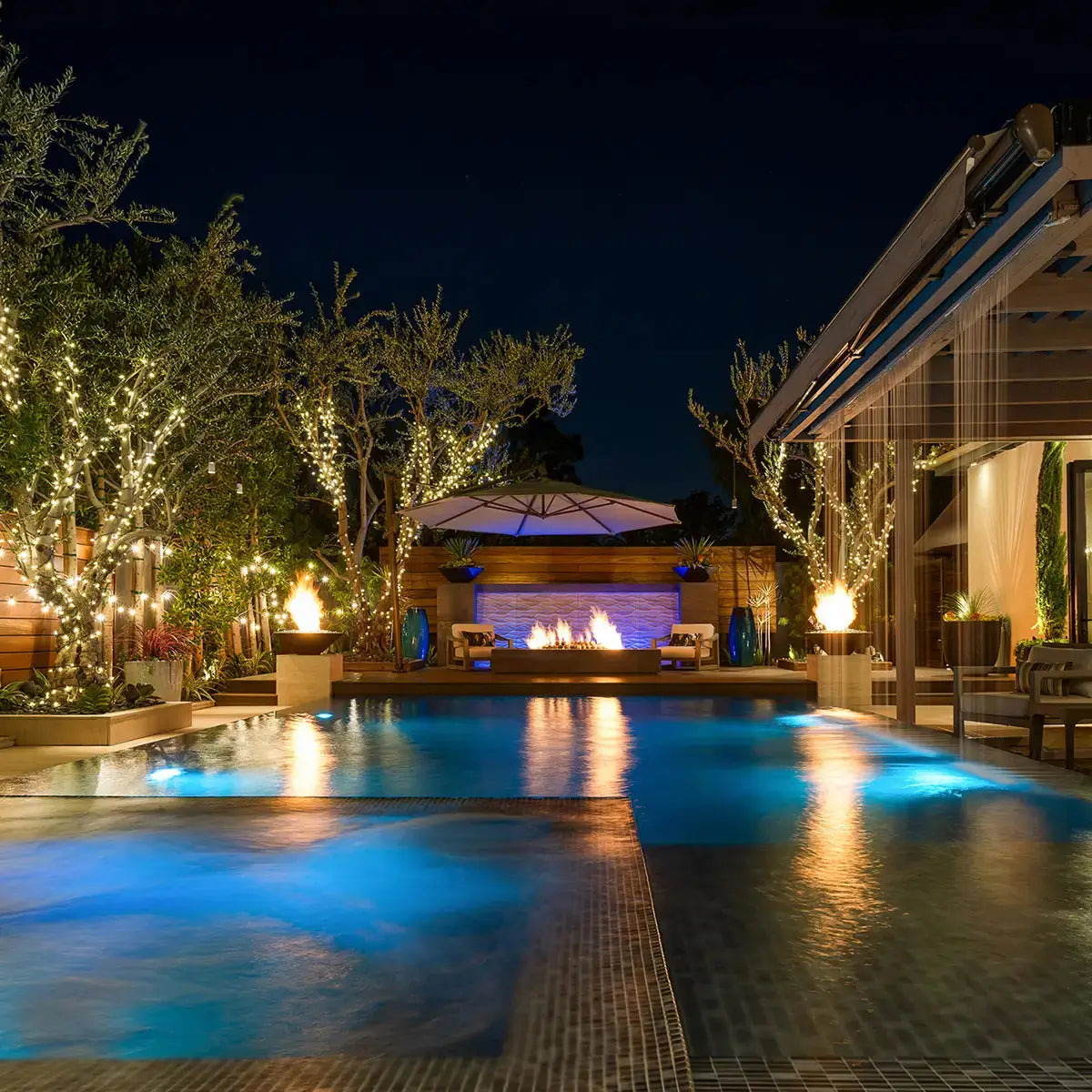 Luxurious pool area at night with glowing fire pit bowls, creating a warm, elegant ambiance for evening relaxation and entertainment.